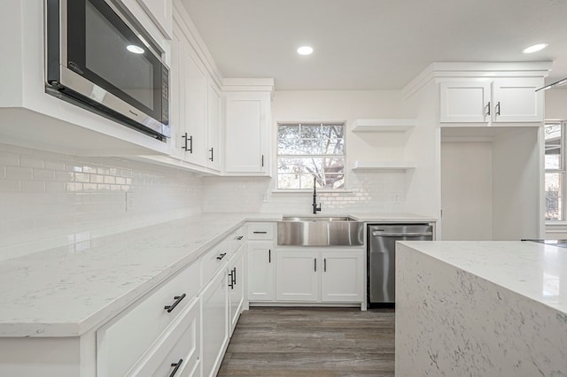 kitchen featuring light stone counters, stainless steel appliances, a sink, white cabinets, and backsplash