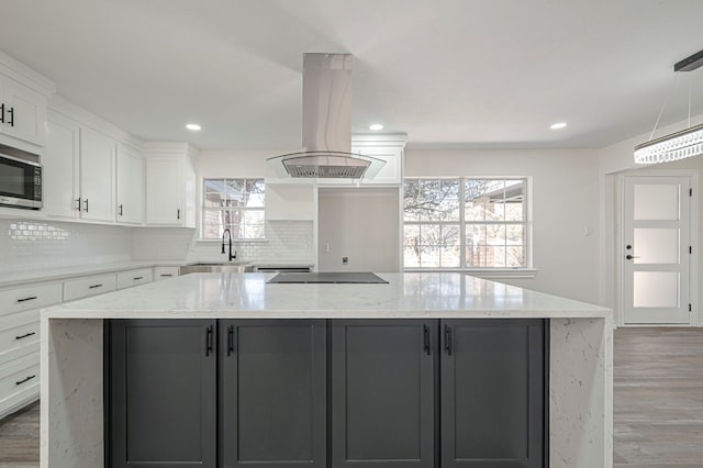 kitchen featuring island exhaust hood, a kitchen island, white cabinetry, stainless steel microwave, and cooktop