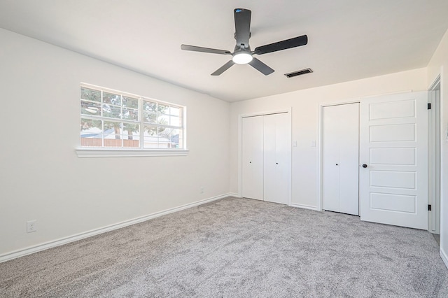 unfurnished bedroom with multiple closets, visible vents, carpet flooring, ceiling fan, and baseboards