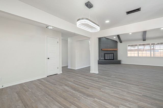 unfurnished living room with baseboards, visible vents, wood finished floors, a fireplace, and beam ceiling