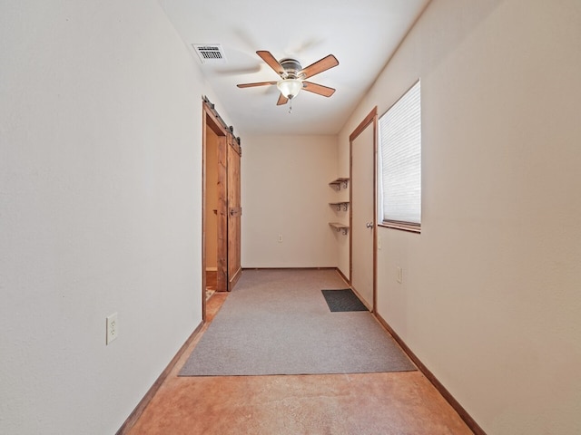 hall with a barn door and light colored carpet