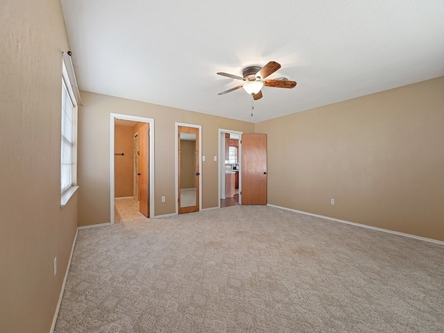 unfurnished bedroom featuring multiple windows, light colored carpet, ceiling fan, and ensuite bath