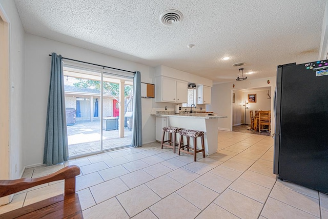 kitchen with white cabinetry, light tile patterned floors, stainless steel fridge, and kitchen peninsula