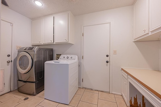 laundry room featuring cabinets, washer and dryer, a textured ceiling, and light tile patterned flooring