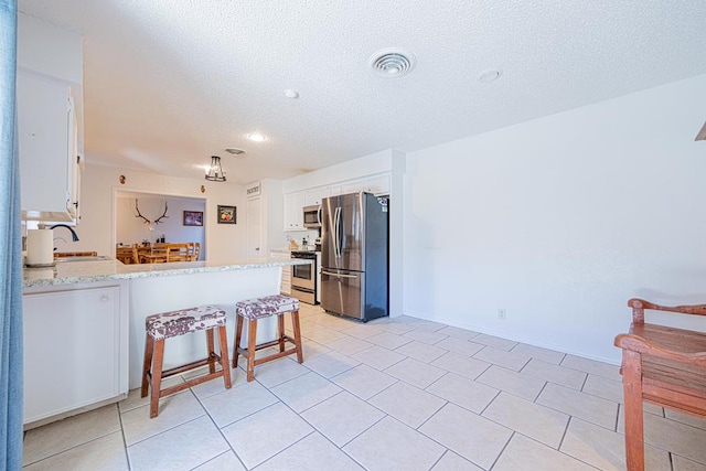 kitchen featuring light tile patterned floors, a breakfast bar area, appliances with stainless steel finishes, white cabinets, and kitchen peninsula