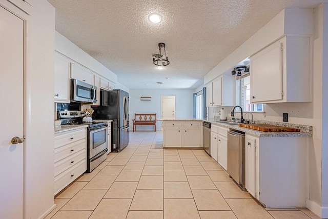 kitchen with sink, light tile patterned floors, stainless steel appliances, a textured ceiling, and white cabinets