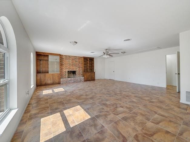 unfurnished living room with built in shelves, ceiling fan, and a brick fireplace