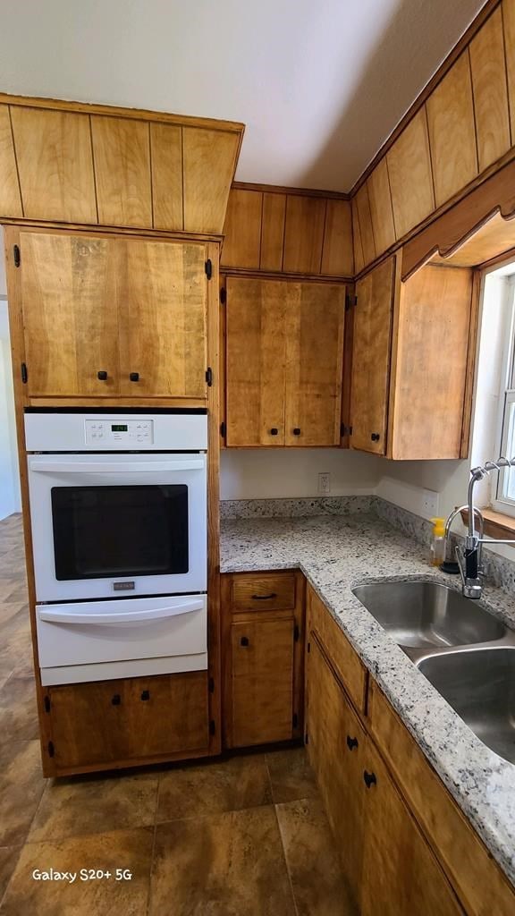 kitchen with white oven, light stone counters, and sink