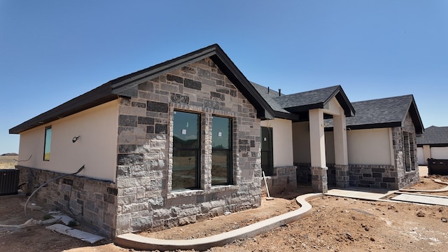view of front of property with central air condition unit, a shingled roof, stucco siding, and stone siding