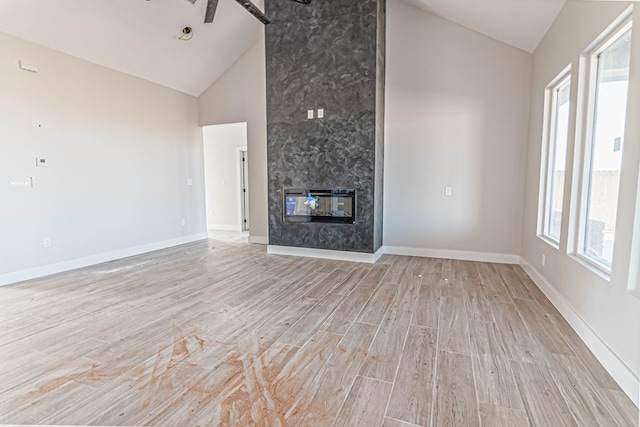 unfurnished living room with a healthy amount of sunlight, high vaulted ceiling, a fireplace, and light wood finished floors