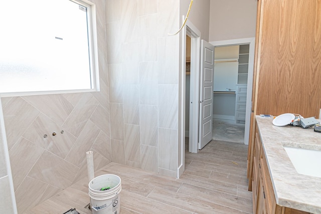 full bathroom with a walk in closet, plenty of natural light, vanity, and wood finished floors