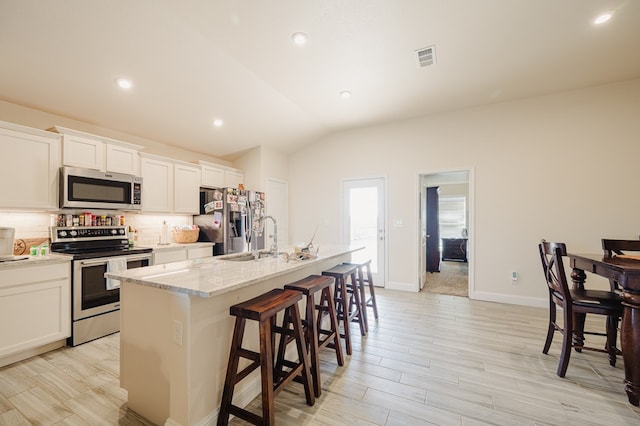 kitchen featuring tasteful backsplash, a center island with sink, a kitchen bar, appliances with stainless steel finishes, and a sink