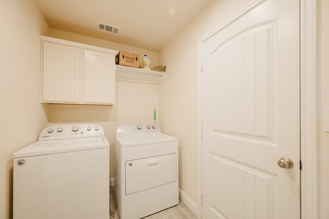 clothes washing area featuring washer and clothes dryer, visible vents, and cabinet space