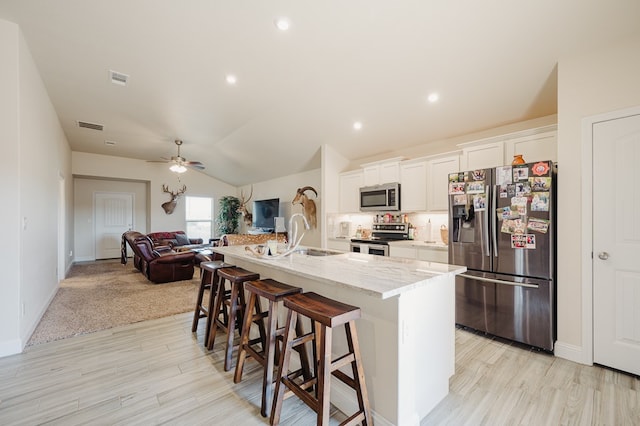 kitchen with visible vents, a sink, a kitchen bar, stainless steel appliances, and a kitchen island with sink