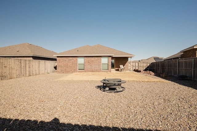 back of property with brick siding, a fire pit, a fenced backyard, and roof with shingles