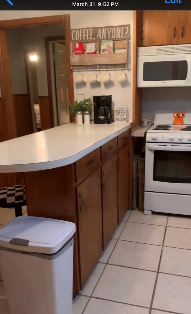 kitchen featuring white appliances, a peninsula, light countertops, and light tile patterned flooring