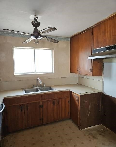 kitchen featuring brown cabinetry, light floors, light countertops, under cabinet range hood, and a sink