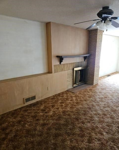 unfurnished living room featuring ceiling fan, a textured ceiling, visible vents, a brick fireplace, and carpet