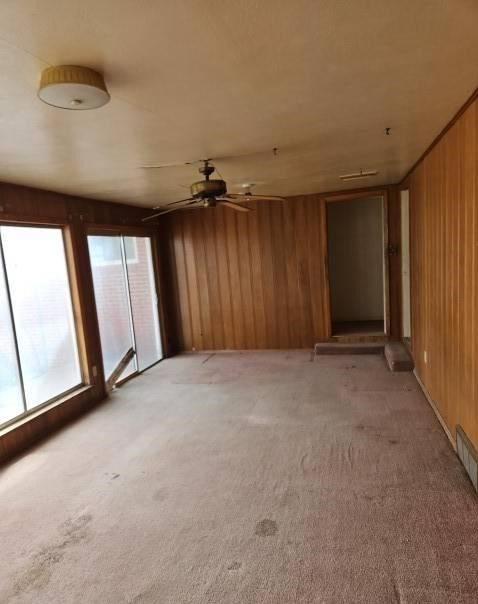 spare room with a ceiling fan, light colored carpet, and wooden walls