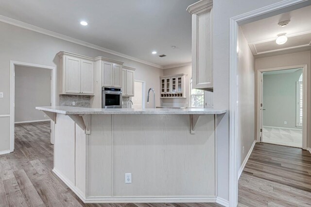 5706 Devlin Pl, Midland, TX 79707 - kitchen featuring oven, light countertops, a breakfast bar area, light wood-type flooring, and ornamental molding