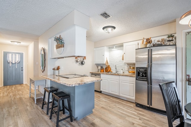 4906 San Antonio Ave, Midland, TX 79707 - kitchen featuring stainless steel appliances, a sink, white cabinetry, a breakfast bar area, and a textured ceiling