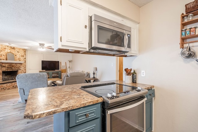 4906 San Antonio Ave, Midland, TX 79707 - kitchen featuring stainless steel appliances, a textured ceiling, white cabinets, a ceiling fan, and a fireplace