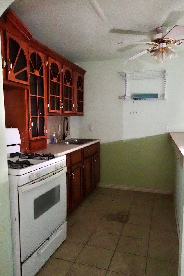 kitchen with white gas stove, tile patterned floors, a sink, a ceiling fan, and glass insert cabinets
