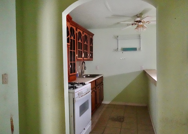 kitchen featuring white gas stove, arched walkways, a ceiling fan, light tile patterned flooring, and a sink