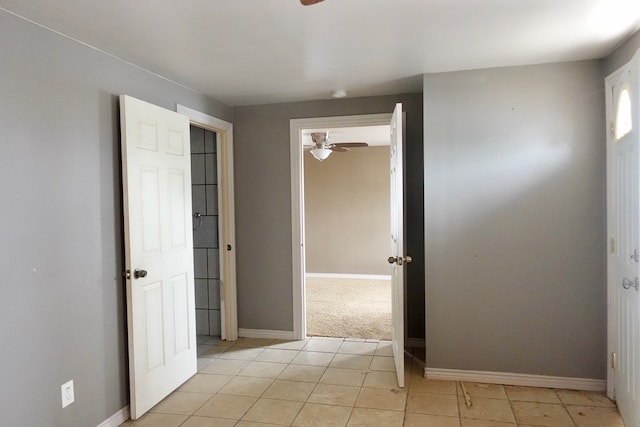 empty room featuring ceiling fan, light tile patterned flooring, baseboards, and light carpet