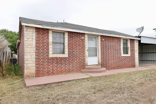 view of front facade with entry steps, brick siding, central AC unit, and an attached carport