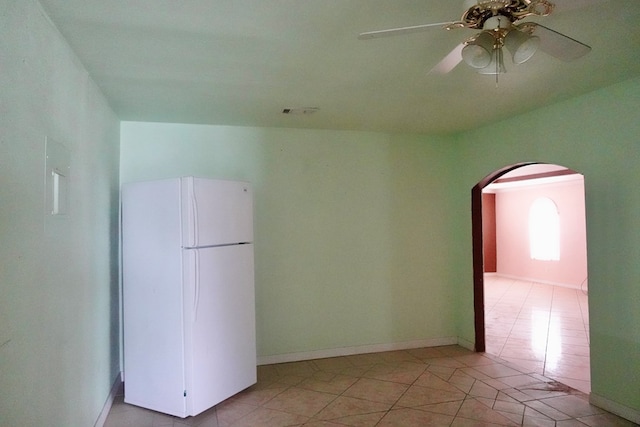 empty room featuring arched walkways, light tile patterned floors, ceiling fan, and baseboards