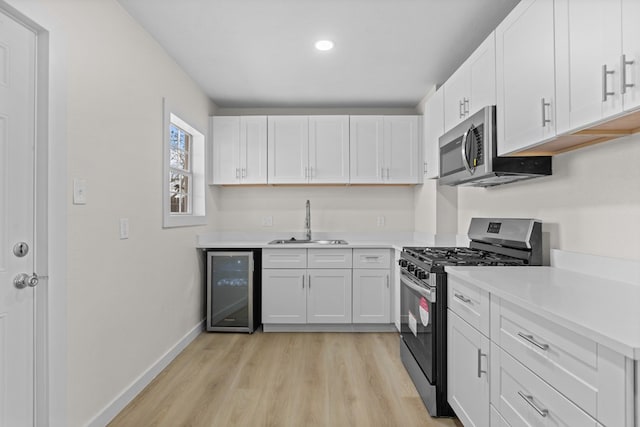 201 E Pine Ave, Midland, TX 79705 - kitchen featuring appliances with stainless steel finishes, white cabinets, wine cooler, light wood finished floors, and a sink