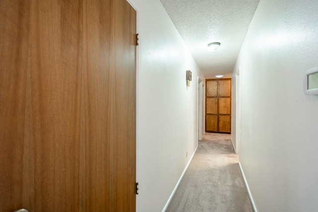 hall featuring light colored carpet and a textured ceiling