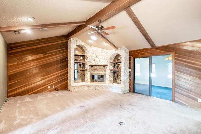 unfurnished living room with a stone fireplace, wooden walls, carpet flooring, ceiling fan, and vaulted ceiling with beams