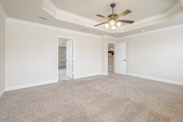 empty room with light carpet, a tray ceiling, visible vents, and crown molding