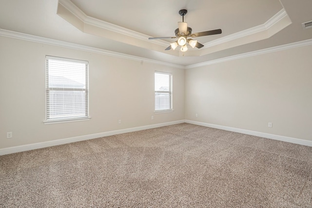 carpeted spare room with ornamental molding, a tray ceiling, visible vents, and baseboards