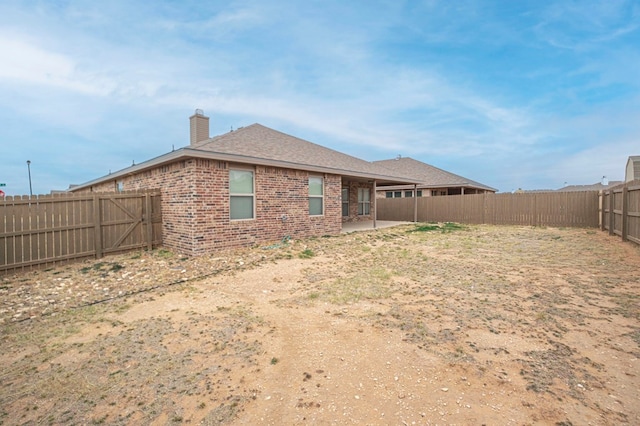 rear view of house with a patio area, a fenced backyard, a chimney, and brick siding