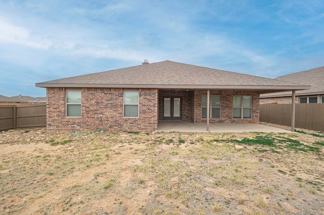 back of property with brick siding, a patio, a fenced backyard, and roof with shingles