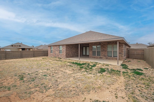 rear view of property featuring a patio area, a fenced backyard, roof with shingles, and brick siding