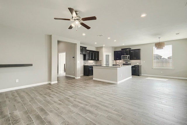 6913 Mcpherson Ln, Midland, TX 79706 - kitchen featuring open floor plan, stainless steel microwave, ceiling fan, backsplash, and light wood-type flooring