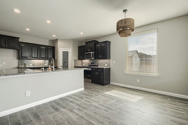 6913 Mcpherson Ln, Midland, TX 79706 - kitchen featuring appliances with stainless steel finishes, tasteful backsplash, dark cabinetry, light wood-style floors, and recessed lighting