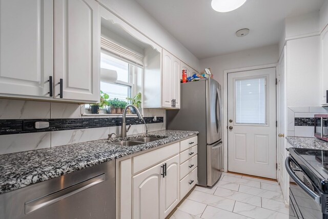 kitchen with marble finish floor, dark stone counters, a sink, backsplash, and stainless steel appliances
