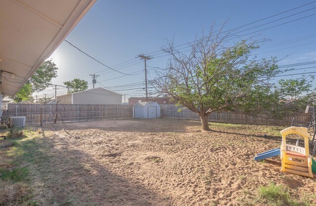 view of yard with a storage unit, a fenced backyard, central AC unit, and an outdoor structure