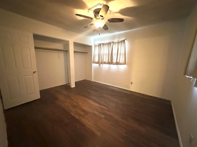 unfurnished bedroom featuring two closets, dark hardwood / wood-style floors, and ceiling fan