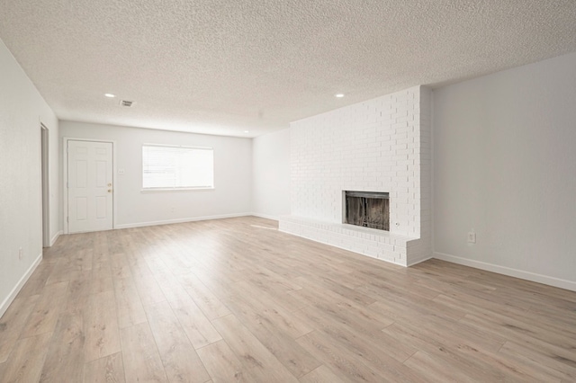 unfurnished living room with a brick fireplace, a textured ceiling, and light wood-type flooring