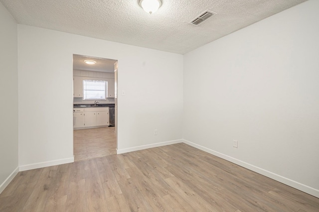 spare room featuring sink, a textured ceiling, and light hardwood / wood-style floors