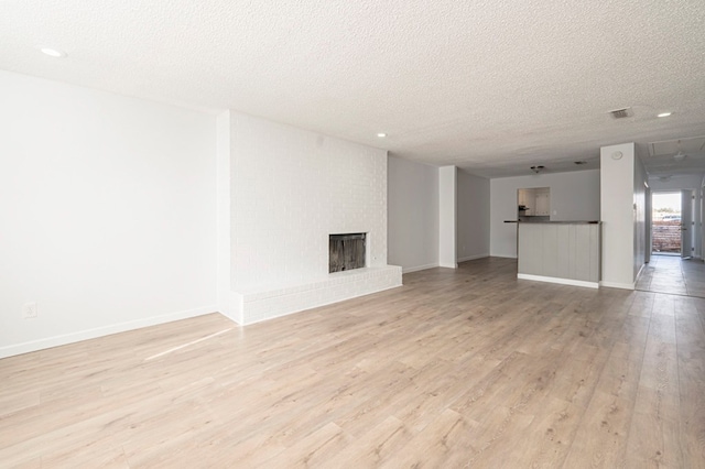 unfurnished living room featuring a brick fireplace, a textured ceiling, and light wood-type flooring