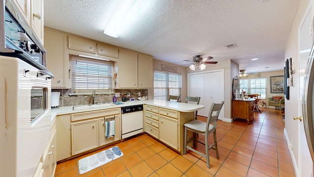 kitchen featuring white appliances, a peninsula, a ceiling fan, cream cabinetry, and a sink
