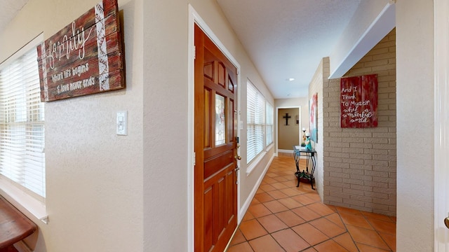 corridor with light tile patterned floors, brick wall, and a healthy amount of sunlight