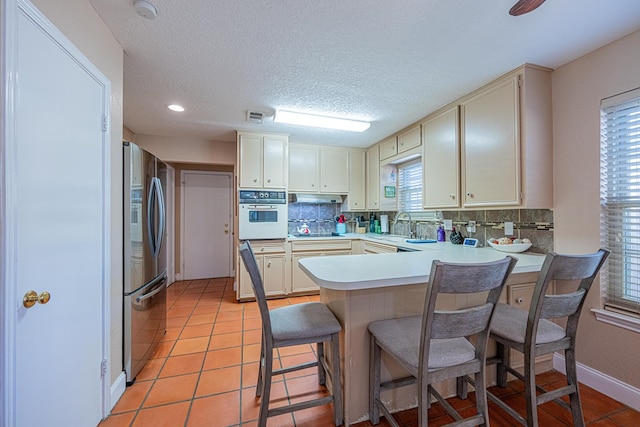 kitchen featuring stainless steel fridge with ice dispenser, a peninsula, white oven, and decorative backsplash